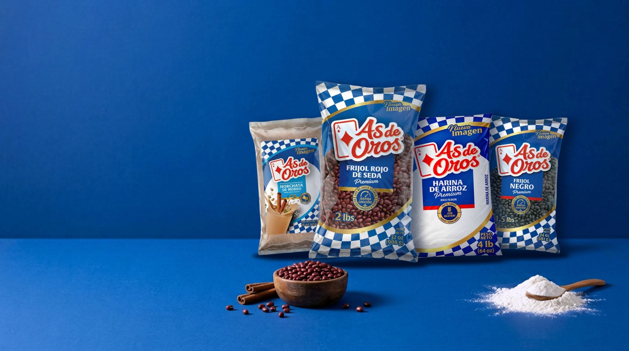 As de Oros packages of horchata de morro, red silk beans (rojo de seda), rice flour and black beans on a blue table, with a bowl of beans, cinnamon and a small mound of rice flour with a wooden spoon.