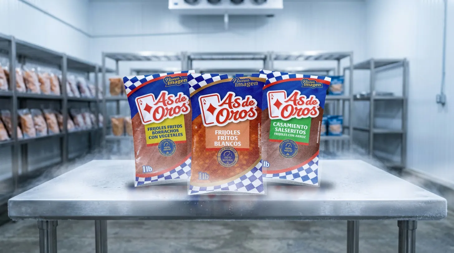 Three frozen As de Oros packages (refried borracho beans, refried white beans and casamiento) on a steel table in a cold room.