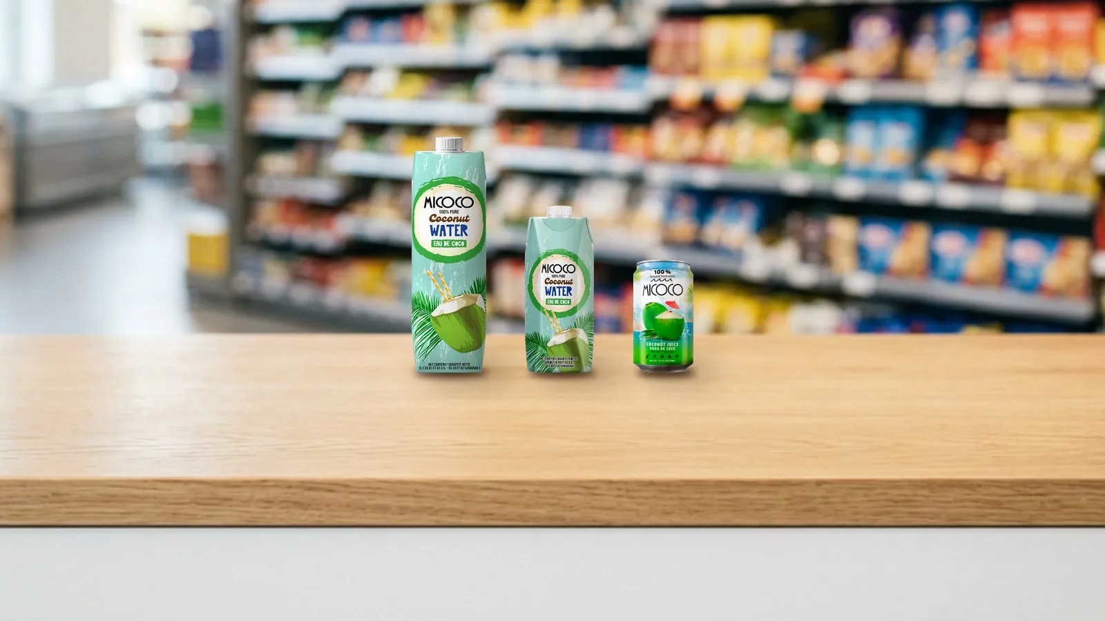 On a wooden supermarket counter, lined up from tallest to shortest, MICOCO coconut water in a 1-liter carton, a 500 ml carton and a 310 ml can.